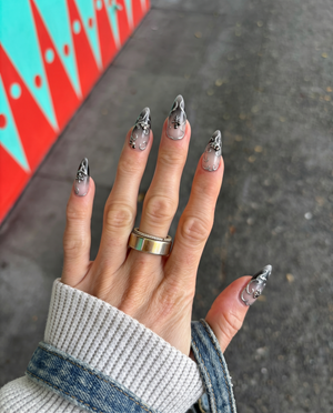 A set of stiletto press-on nails with a dark grey ombre gradient and silver filigree embellishments.