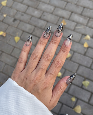 A set of stiletto press-on nails with a dark grey ombre gradient and silver filigree embellishments.