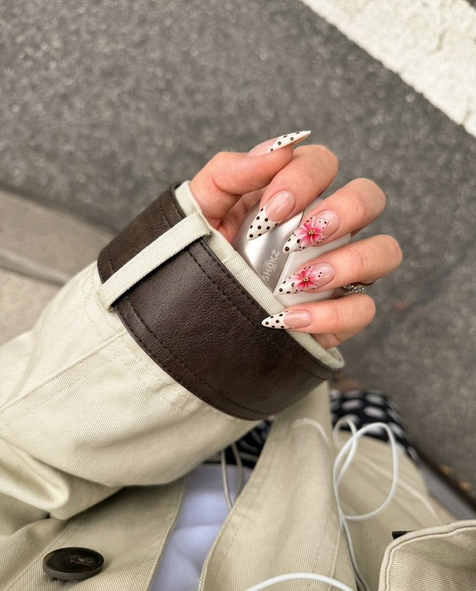 A set of press-on nails featuring a nude base, white French tips with black polka dots, and pink 3D floral accents.