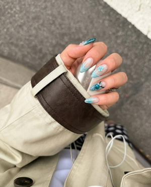 A set of teal-toned press-on nails featuring ocean motifs like a starfish, jellyfish, seashell, and sea turtle with rhinestone accents.