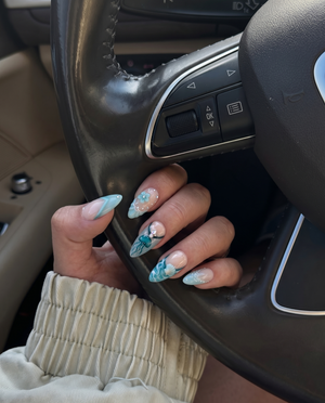 A set of teal-toned press-on nails featuring ocean motifs like a starfish, jellyfish, seashell, and sea turtle with rhinestone accents.
