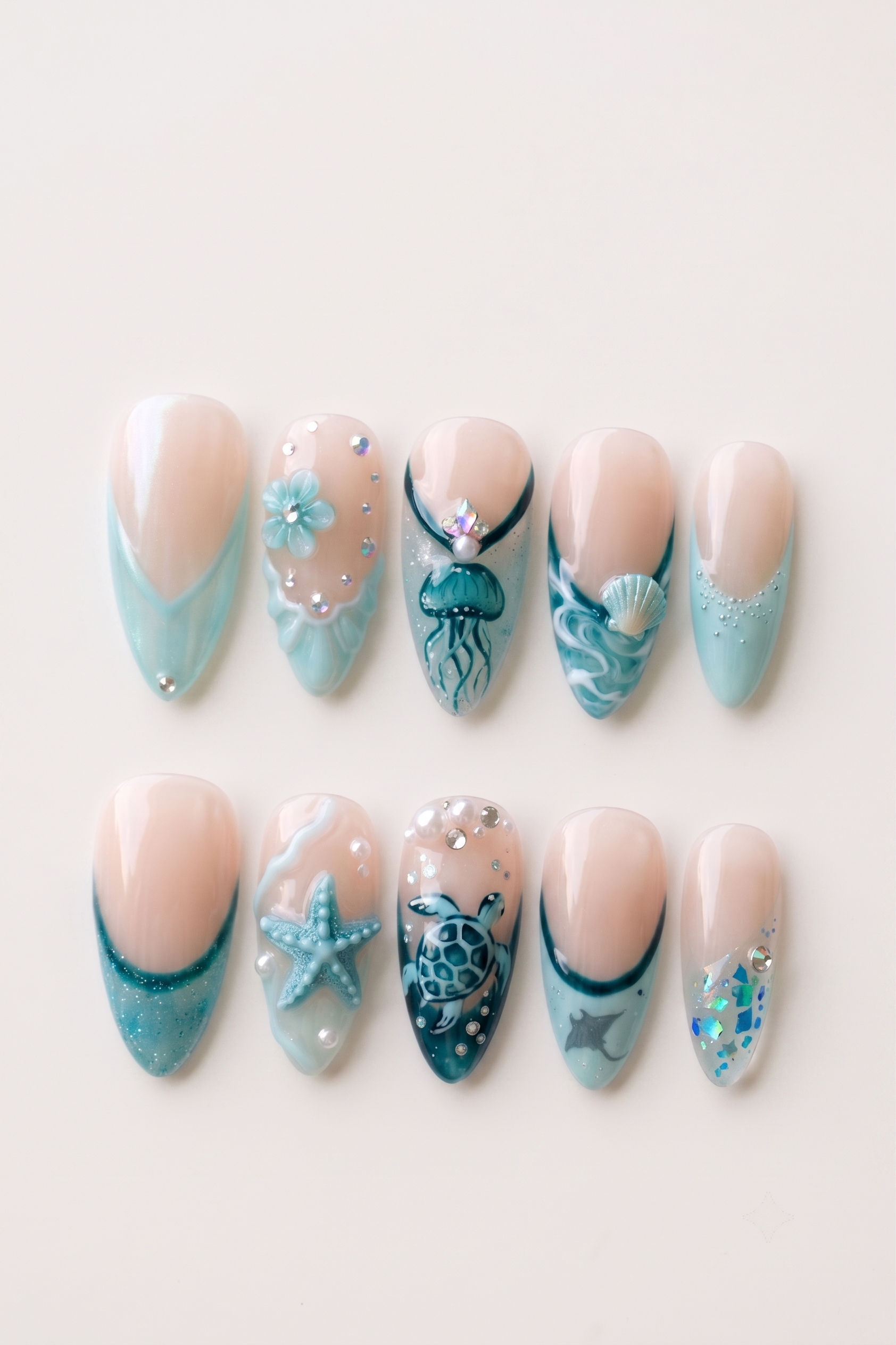A set of teal-toned press-on nails featuring ocean motifs like a starfish, jellyfish, seashell, and sea turtle with rhinestone accents.