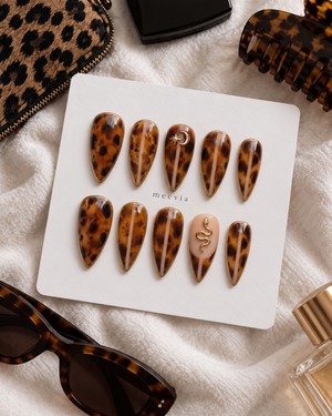 Glossy tortoiseshell press-on nails with gold edging, moon and star details, and a snake accent